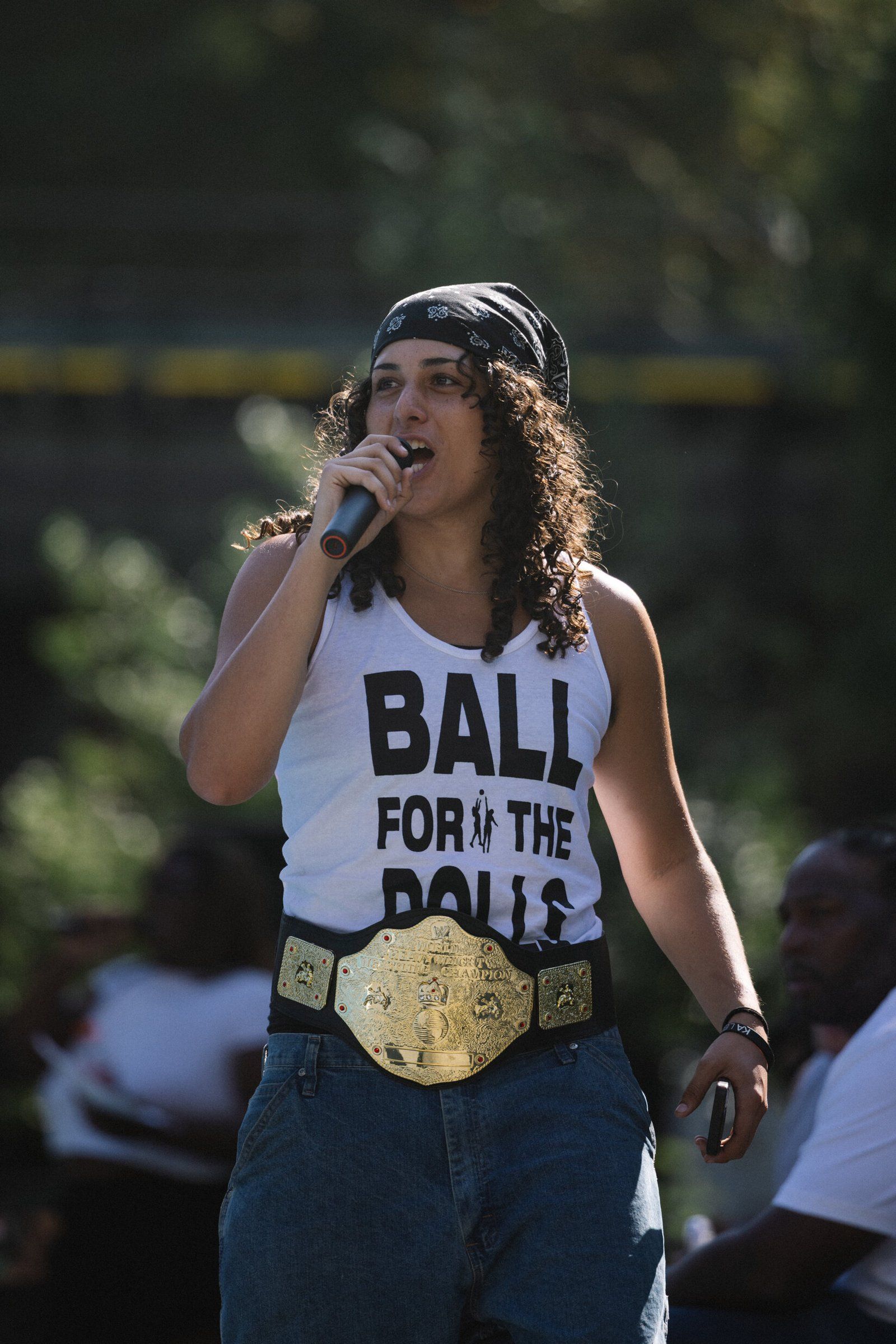 Founder of Basketdolls Devin Myers holding a mic and speaking. Vest reads - "Ball for the Dolls"