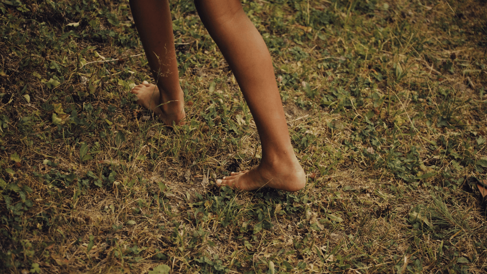  Close-up of bare feet walking on grassy ground, embodying a natural outdoor experience.