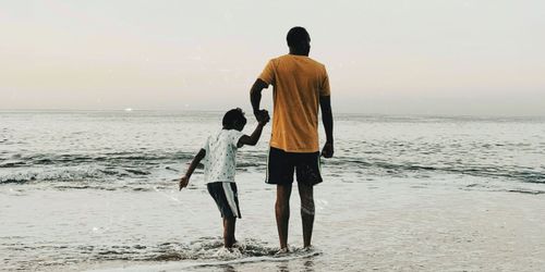 A man and young boy holding hands along the shoreline