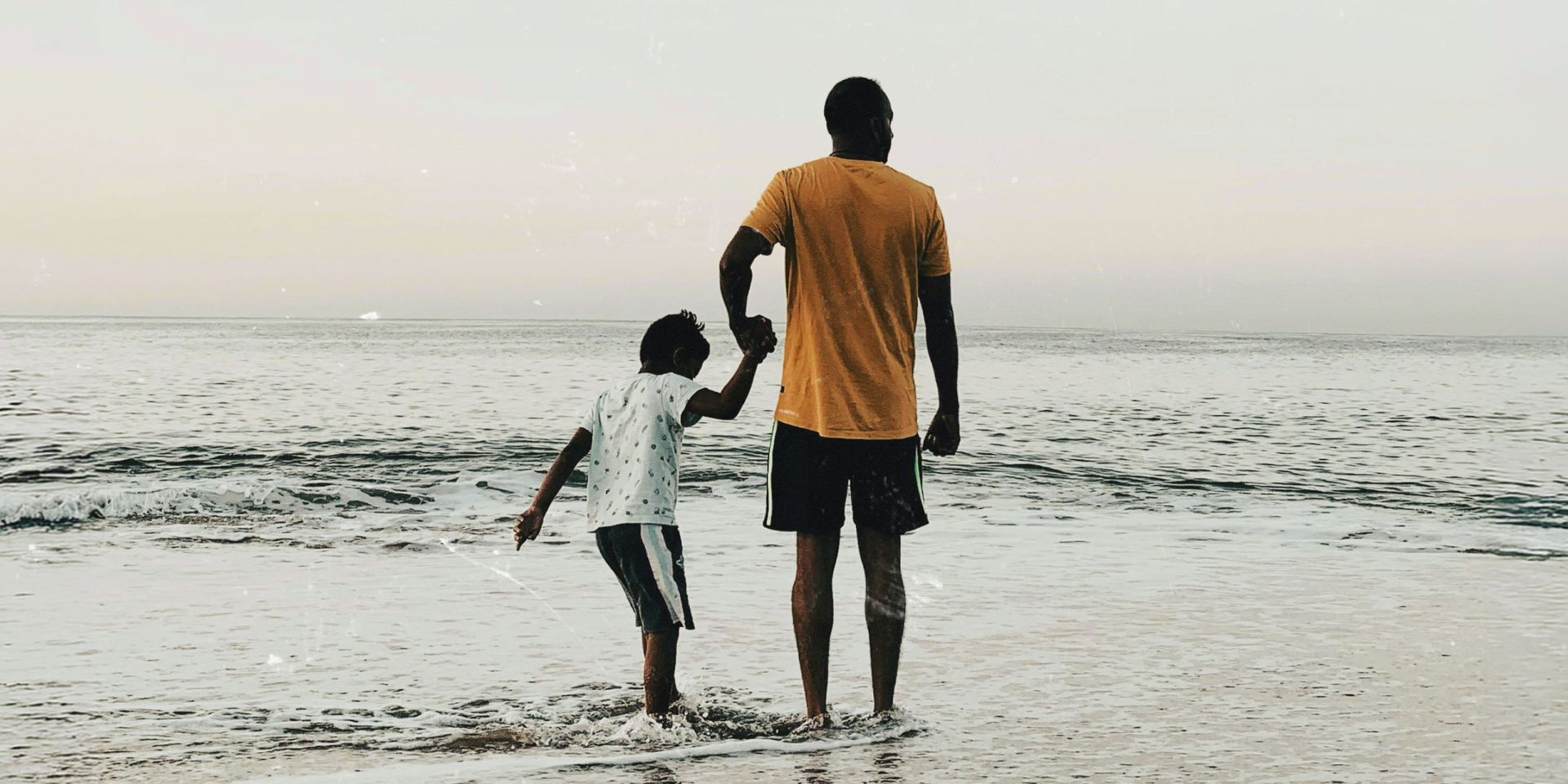 A man and young boy holding hands along the shoreline